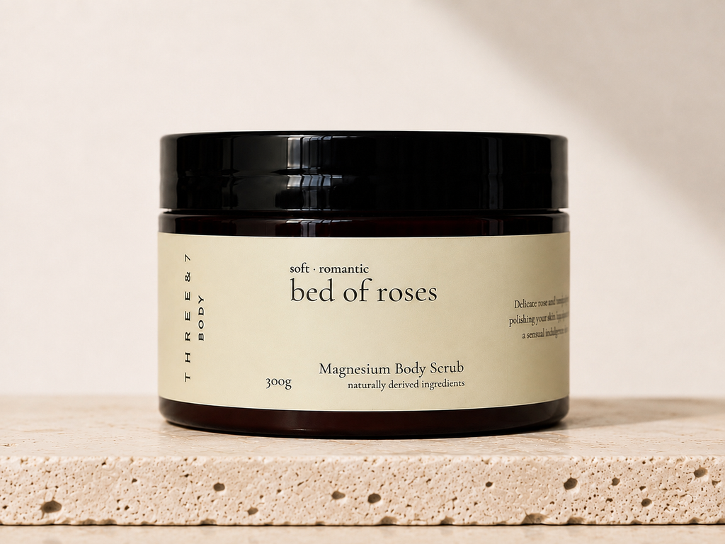 THREE & 7 bed of roses Magnesium Body Scrub 300g in amber jar on a travertine stone surface.