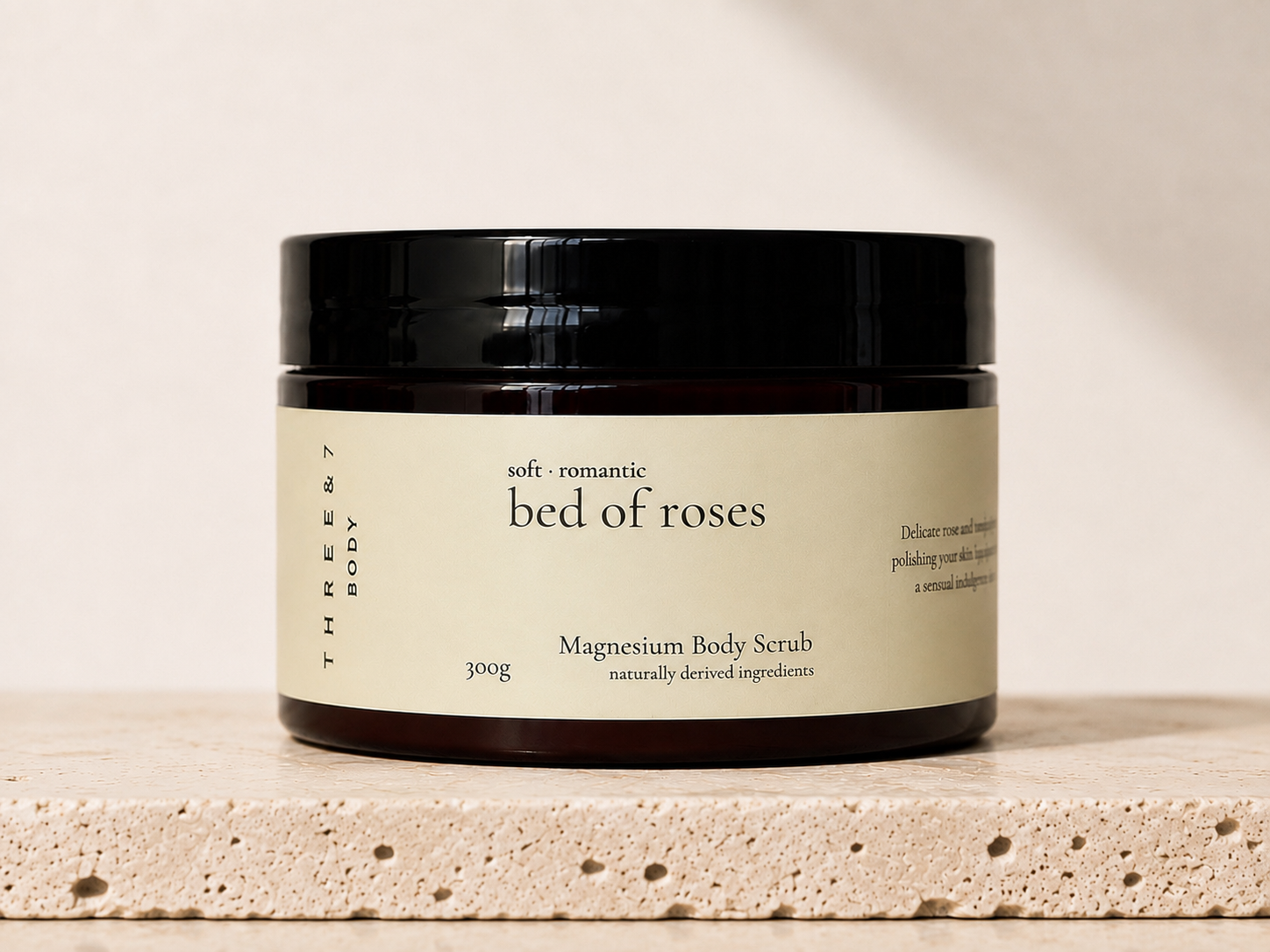 THREE & 7 bed of roses Magnesium Body Scrub 300g in amber jar on a travertine stone surface.